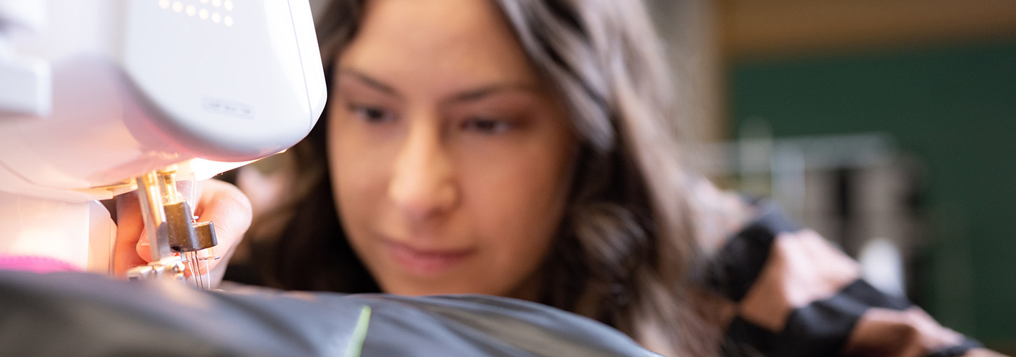 Close-up of a sewing machine with a woman in the background.