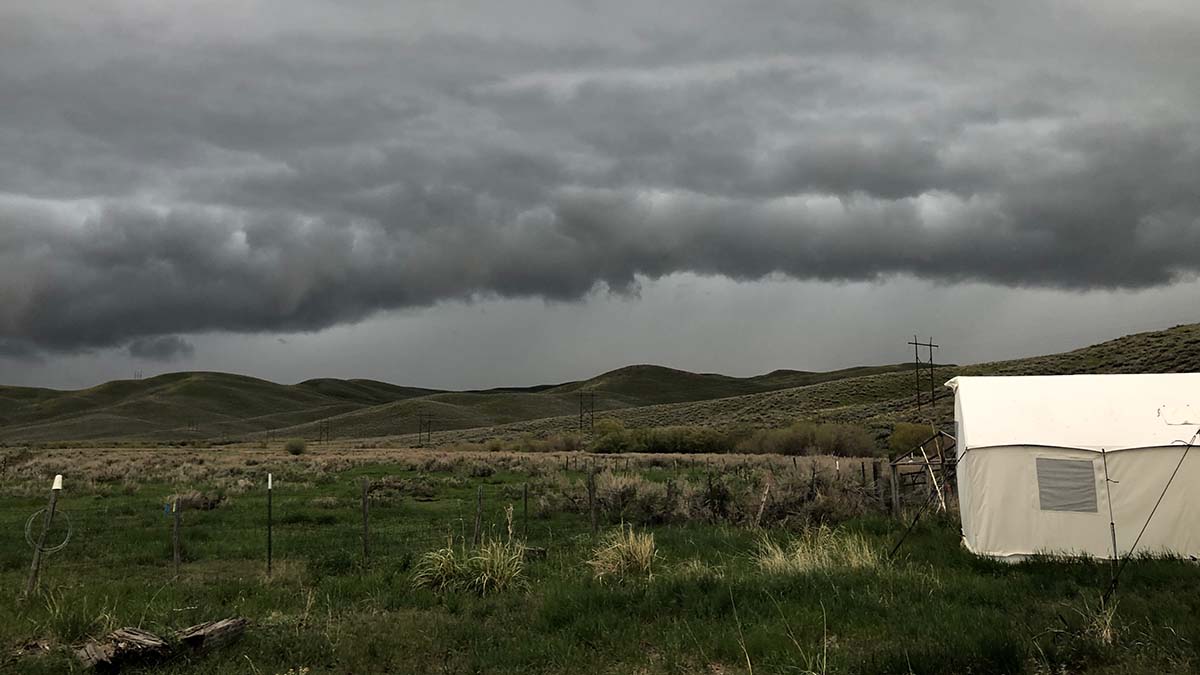 A tent sits in a field as a thunderstorm rolls in.