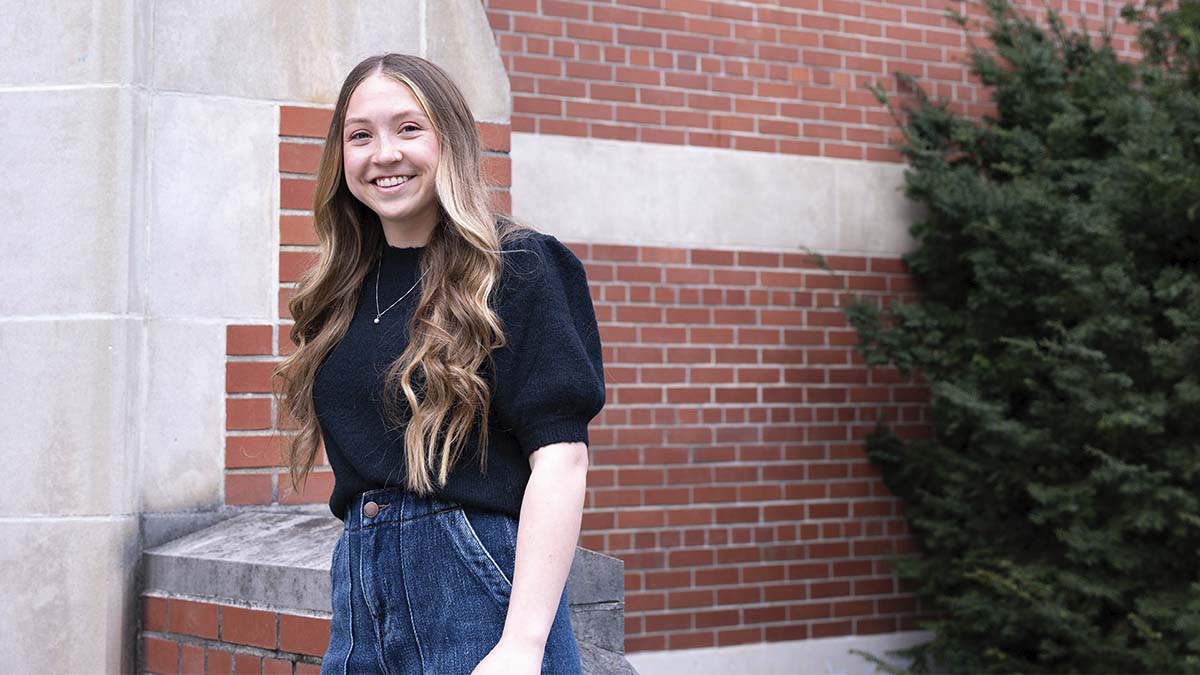 A woman poses next to a brick building on the University of Idaho campus.