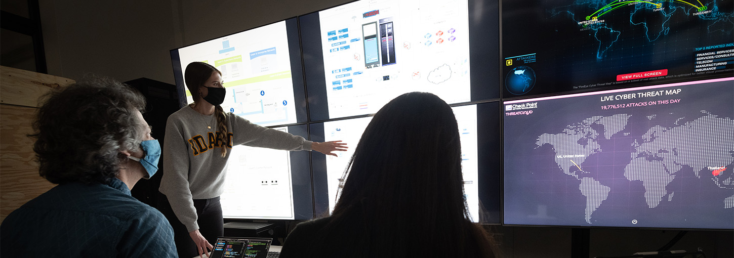 Woman touching multi-media display with two individuals seated.