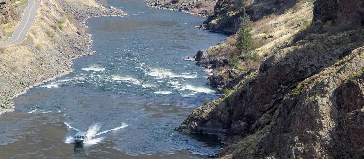 A small boat in the corner leaves a wake in the water between two steep banks.