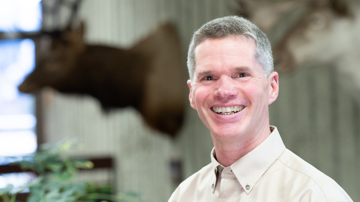 Smiling man stands near mounted elk head