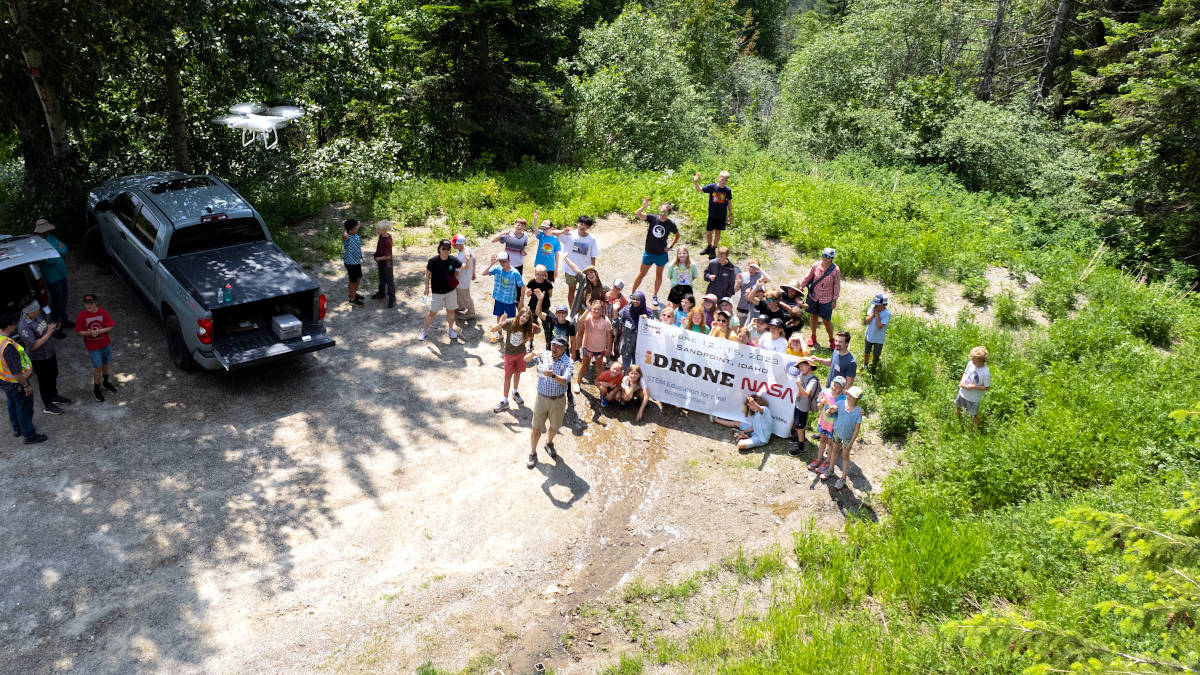 Drone photo of group standing on the ground holding a banner.