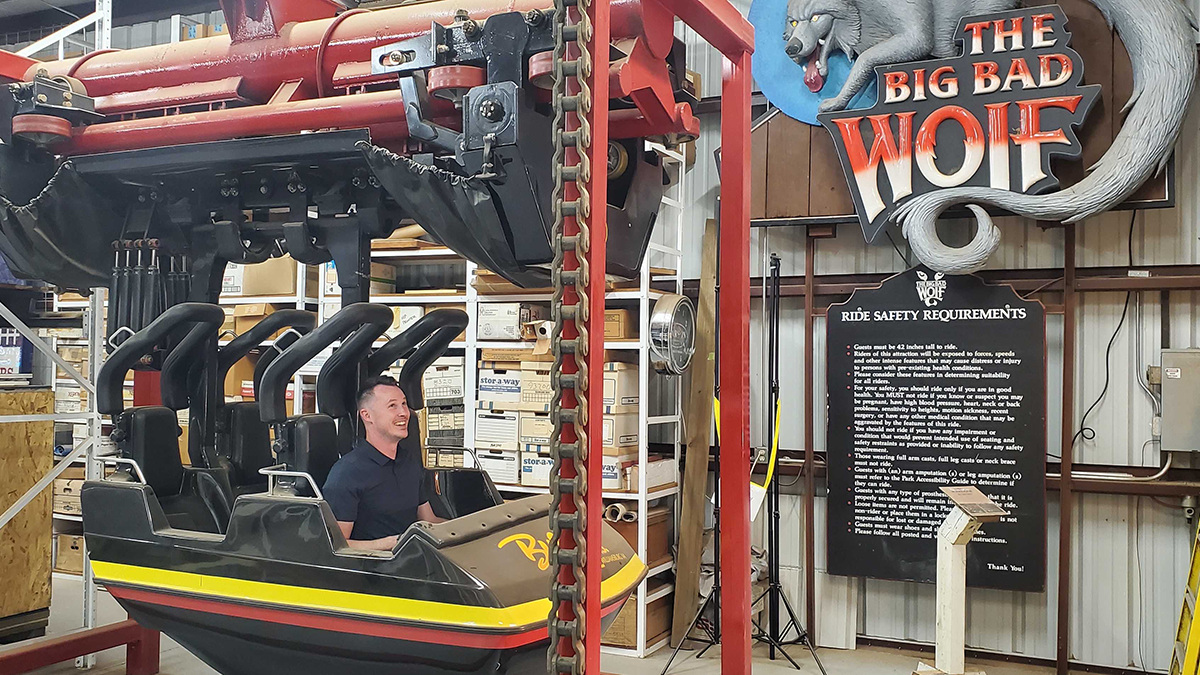 Man sits in black roller coaster train cart. 