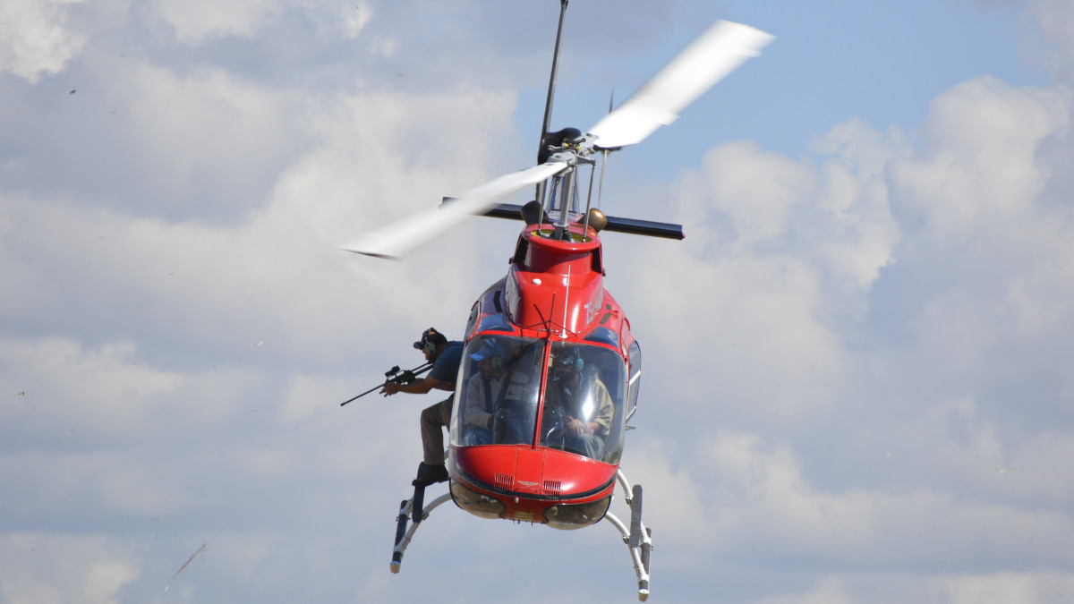 Person with dart gun leaning out of airborne helicopter.